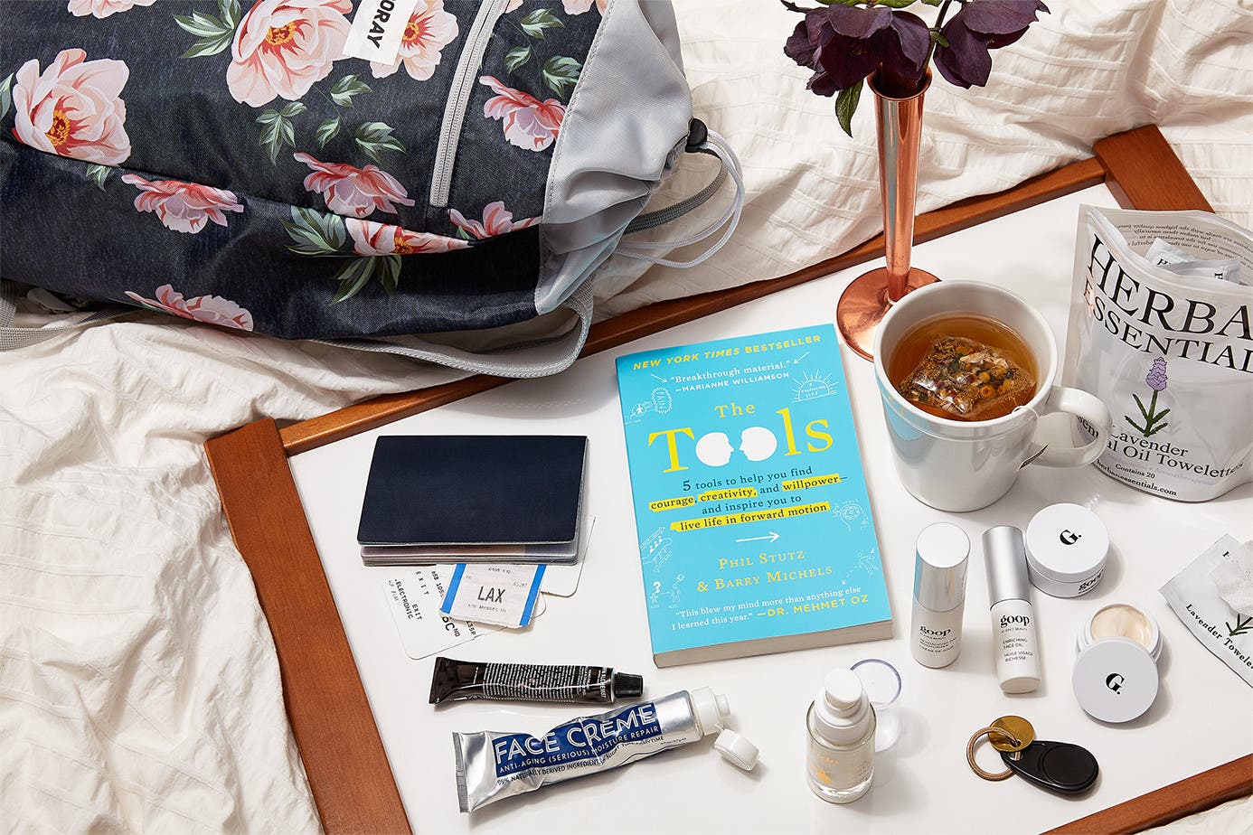 goop travel products sprawled out on a bed sheet.