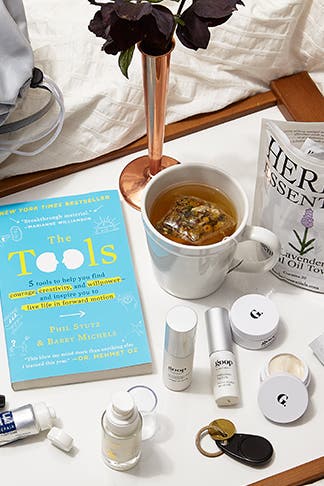 goop travel products sprawled out on a bed sheet.