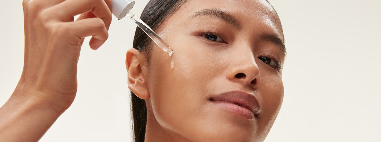 A woman applying an eyedropper of serum to her face.