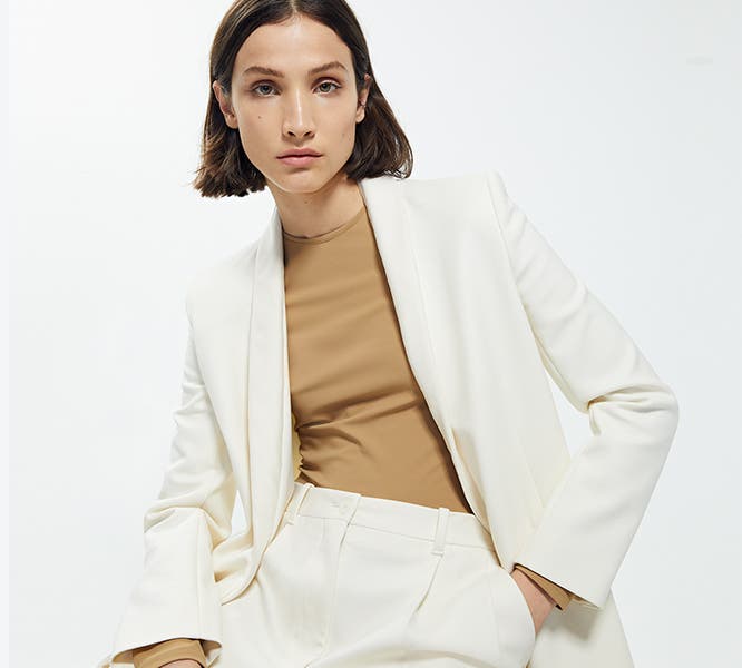 Model wearing beige shirt, white suit jacket and trousers from The Row.