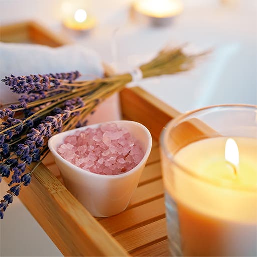 A bundle of lavender, a bowl of bath salts and a lit candle.