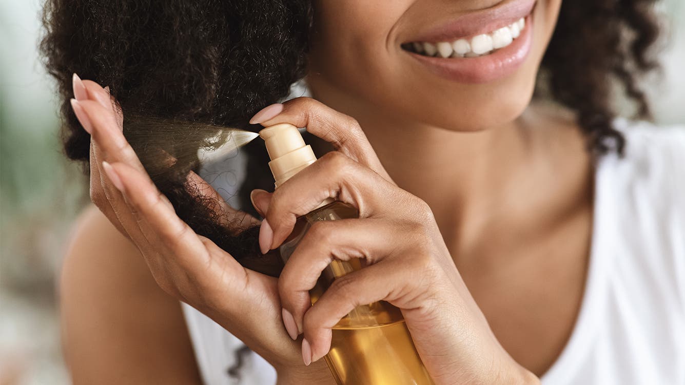 A woman sprays product on her natural hair.