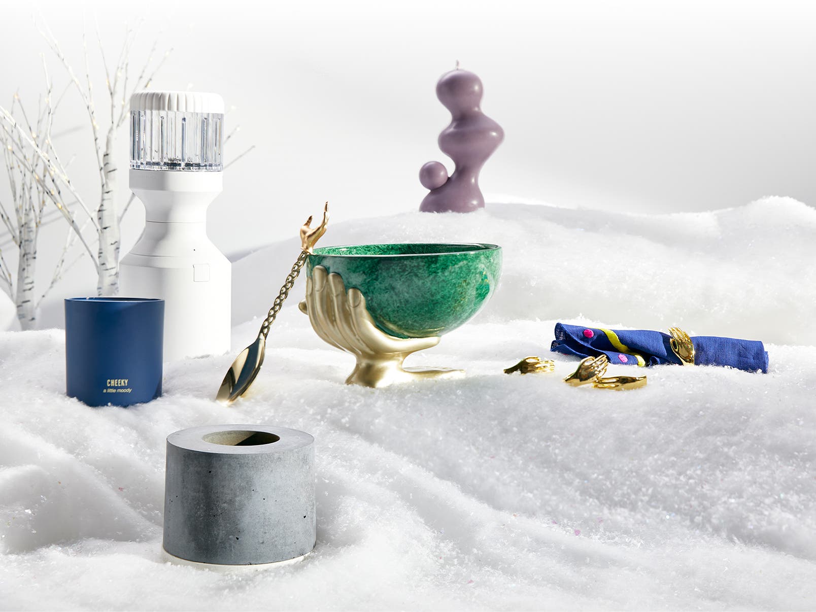 Hashtag Nordstrom Pop. A selection of gifts in the snow including a purple sculptural candle, scented candle, sleek blender; and a green bowl and serving spoon adorned with a golden hand.