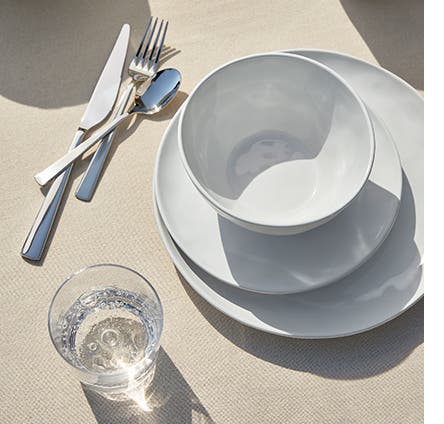 White plates and bowl, a drinking glass and silverware.