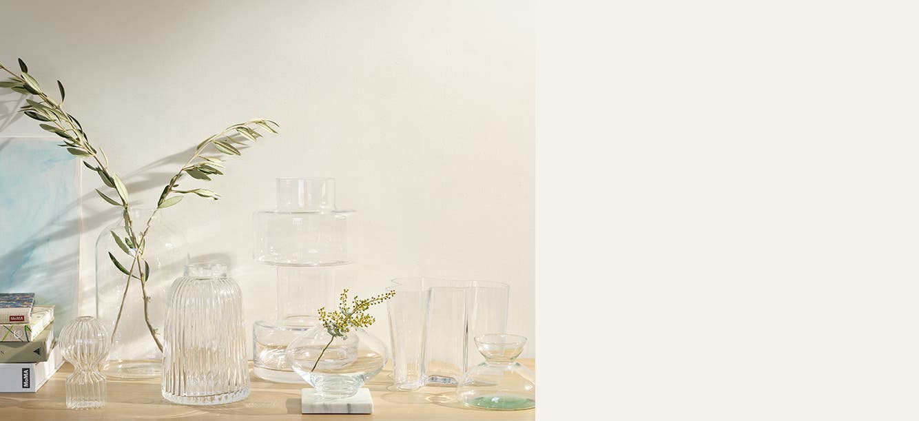 Translucent vases and fresh-cut greens with tonal-colored books.