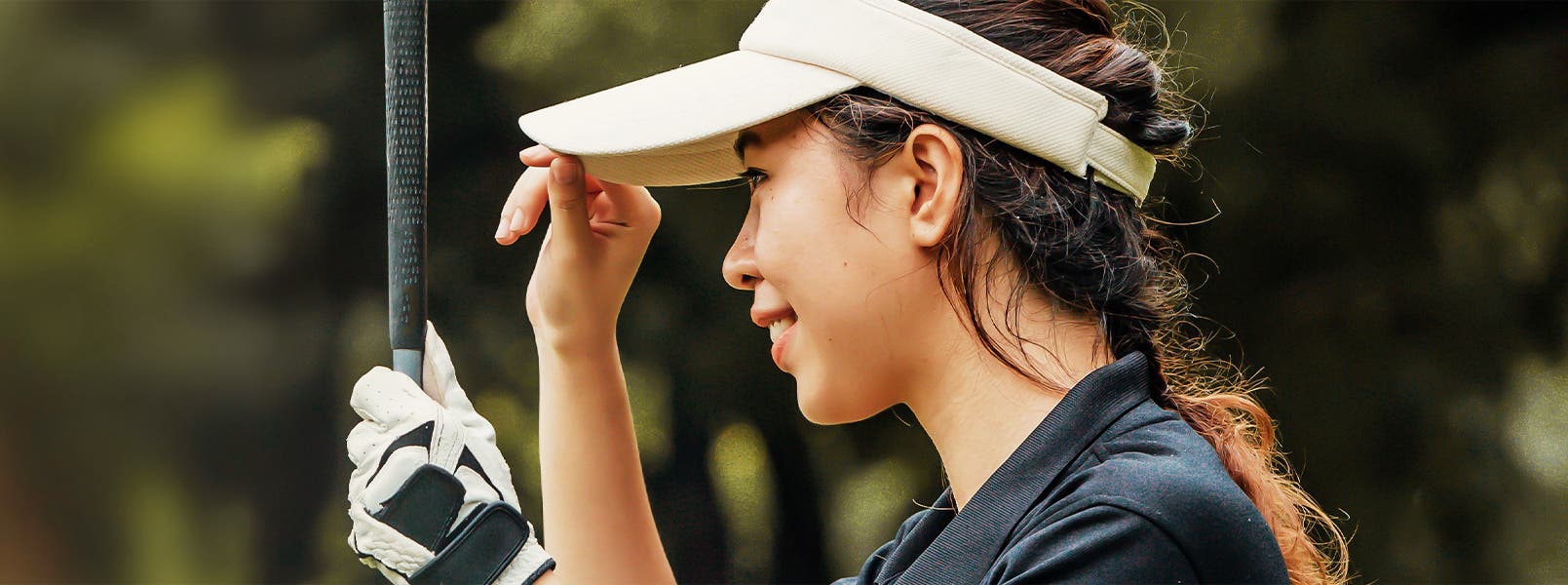Closeup of a woman golfer holding her club wearing a golf glove and visor.