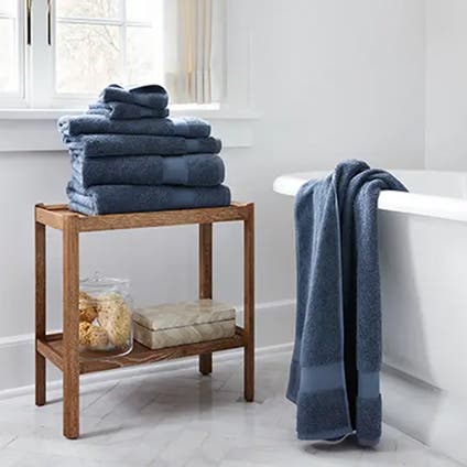 Blue towels folded and stacked on top of each other with another placed on a bathtub.