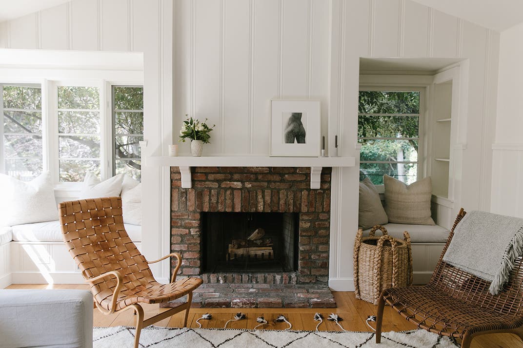 A brick fireplace flanked by two neutral-colored chairs and windows. 