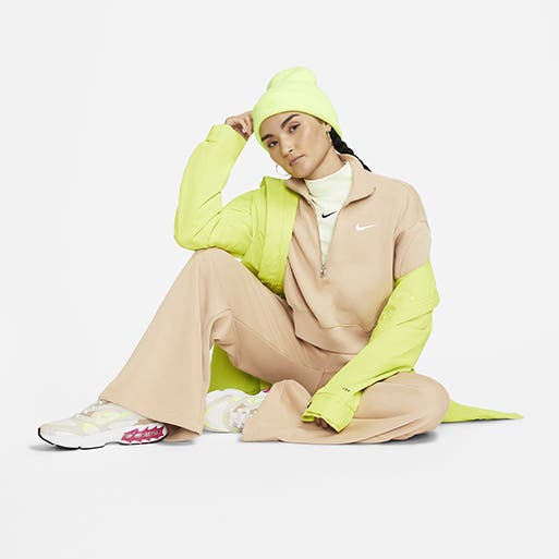 A model wearing a neon coat and beanie with a tan zip-front sweatshirt, tan lounge pants and sneakers.