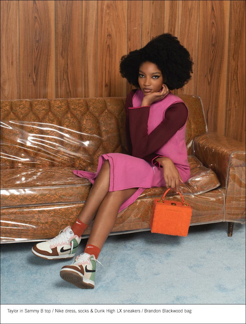Model wearing a top, dress, socks and sneakers holding an orange handbag.