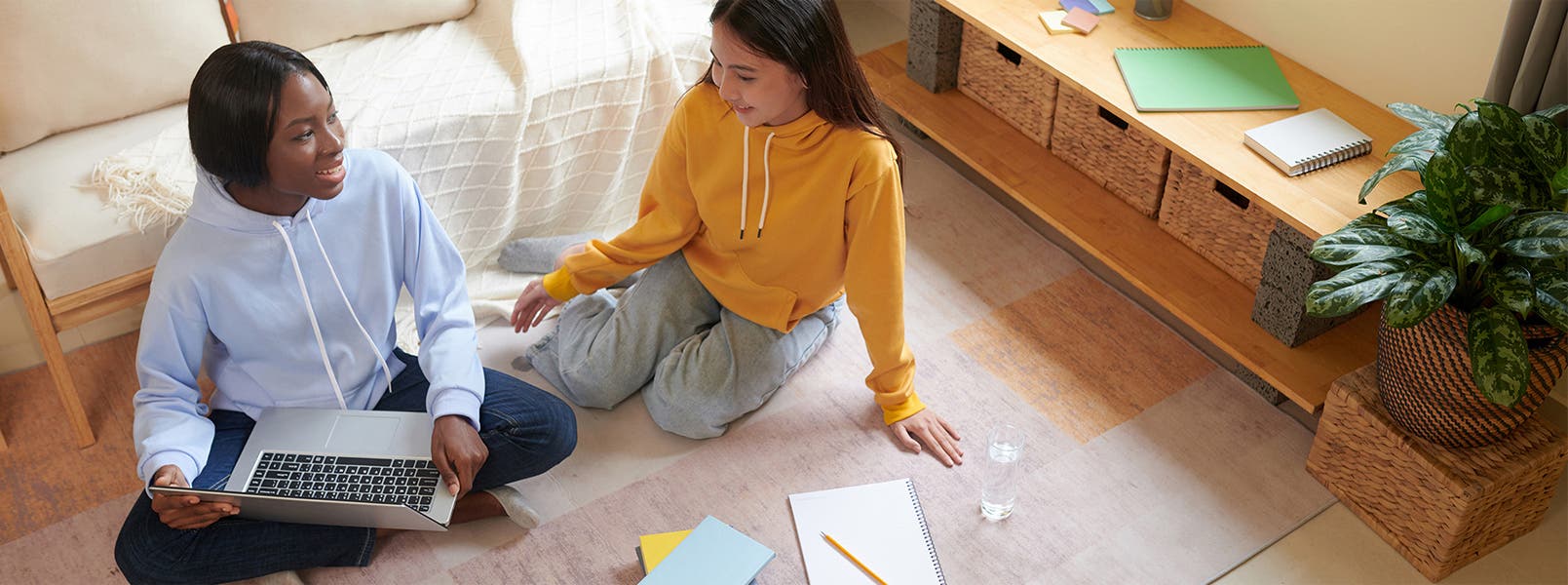 Two young women sitting on the floor with a laptop and notebooks.