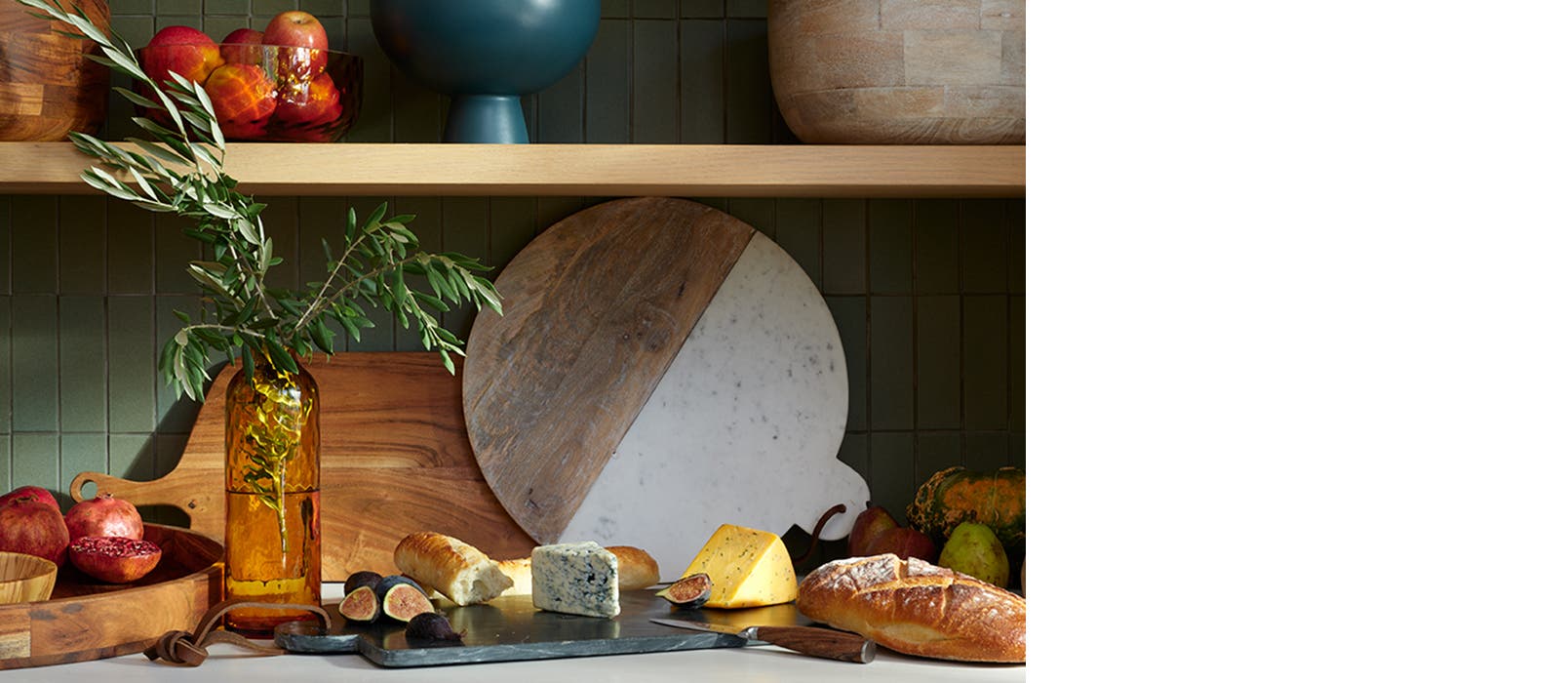 A kitchen counter with cheese, bread, fruit, cutting boards and bowls.
