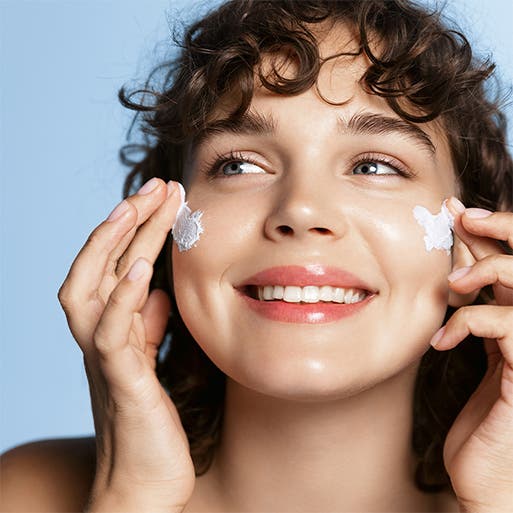 A woman applies moisturizer to her face.