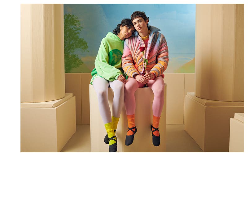 A model in a colorful hoodie and a model in a pastel-striped puffer jacket, both wearing colorful tights and ballet-style shoes.