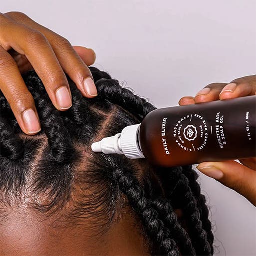 A person applying hair oil to the scalp.