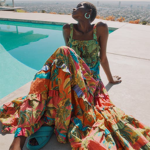Woman in a multicolored print maxi dress sitting poolside.