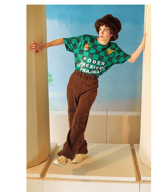 Model wearing green checkerboard T-shirt, sneakers and a brown hat and pants.