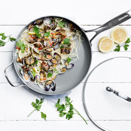 A nonstick pan with pasta, mussels, lemon and herbs.
