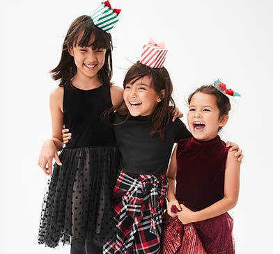 Three children laughing and smiling dressed up in festive dresses.