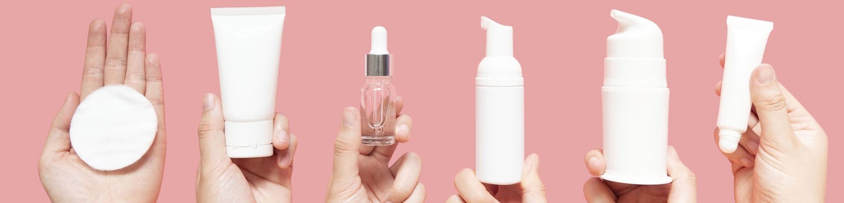 Hands holding up skincare products like face cleanser, serum, moisturizer, and eye cream.