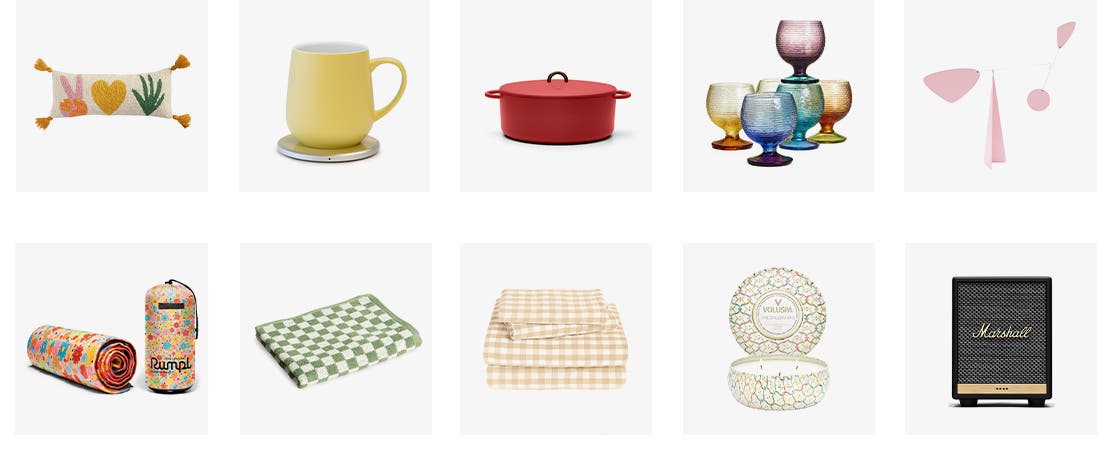 A hooked wool throw pillow with tassels. A yellow mug and warmer set. A red cast-iron pot. Set of 6 multicolored goblets. A pink metal tabletop mobile. A rolled-up puffy blanket. A green checkerboard print hand towel. A cream gingham print sheet set. A three-wick tin candle. A Marshall smart home speaker.
