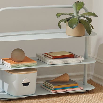 A white entryway rack holding a plant, books and a storage bin.