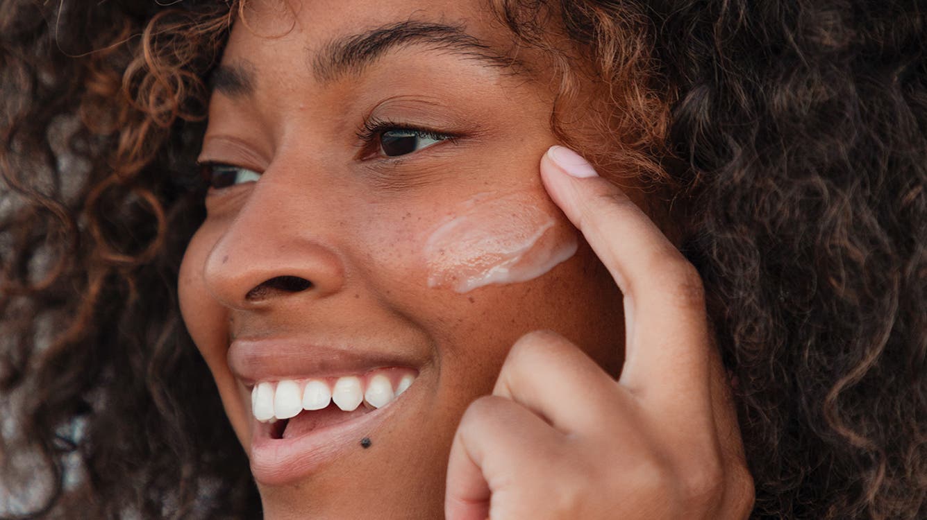A woman applies skin care to her face.