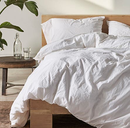 A bed with a rumpled white duvet.
