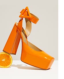 An orange high-heel shoe propped on an orange slice.