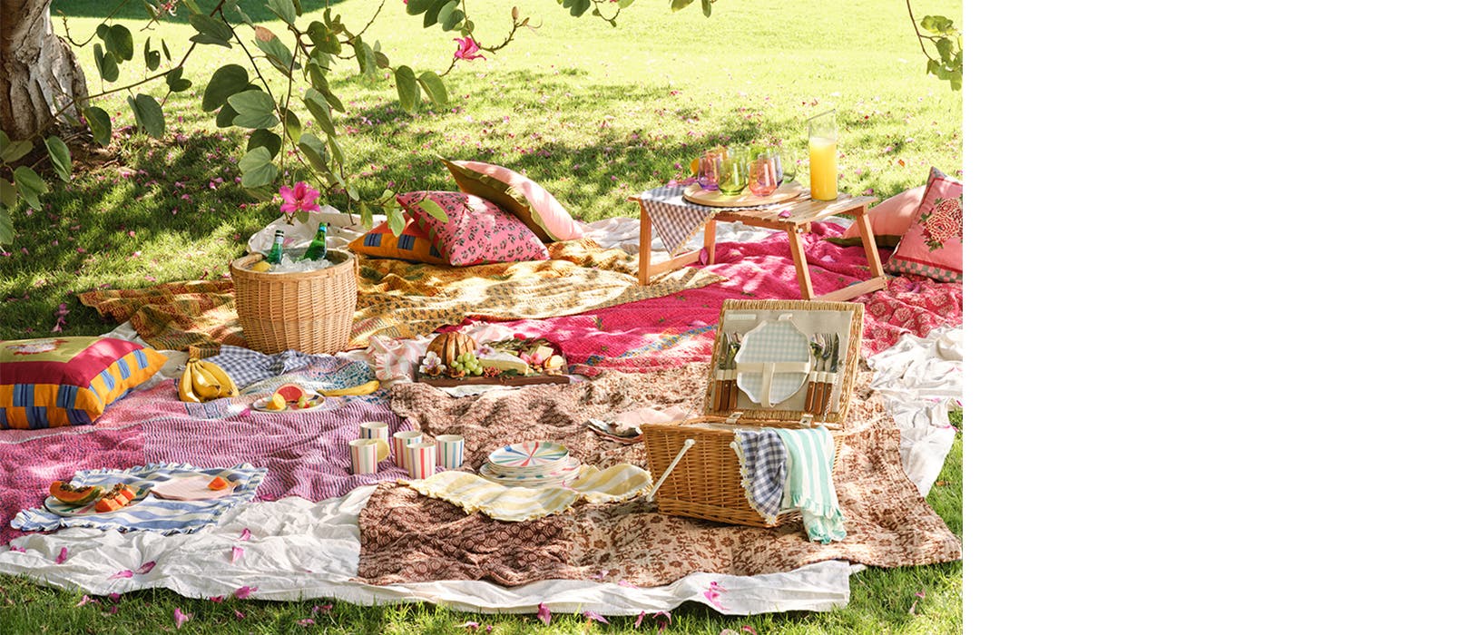 A picnic in the grass with colorful blankets, tablecloths, pillows, tableware and more.