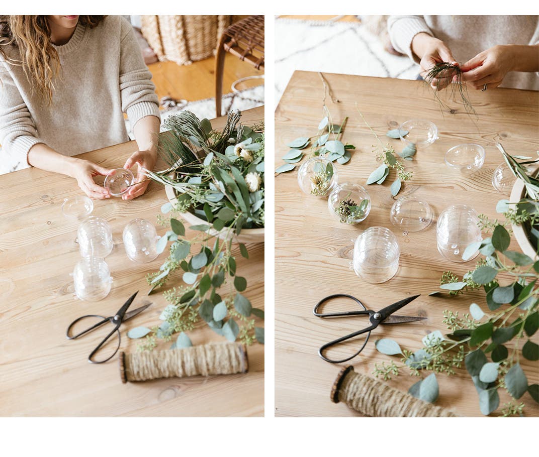 Clear round ornaments, a bowl of greenery, scissors and twine.
