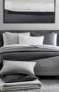 Quilts, sheets and pillows in shades of grey.