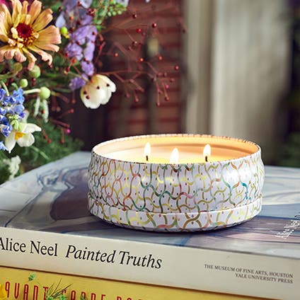 A 3-wick tin candle atop of a stack of books.