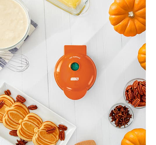 Pumpkins, pumpkin-shaped waffles and an orange waffle maker sit on a table.