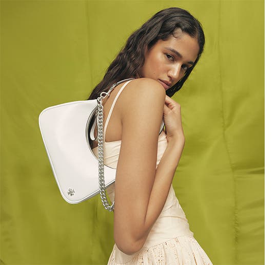 Woman holding a small leather crescent bag in white from Tory Burch.