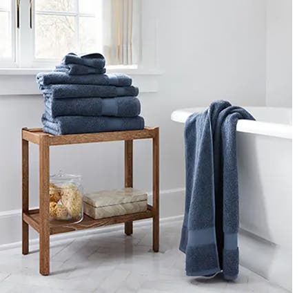 Blue towels folded and stacked on top of each other with another placed on a bathtub.