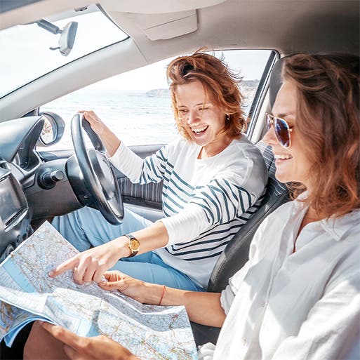 Two women in a car consult a paper map.