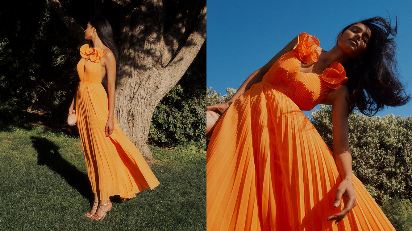 A woman wearing an orange pleated maxi dress.