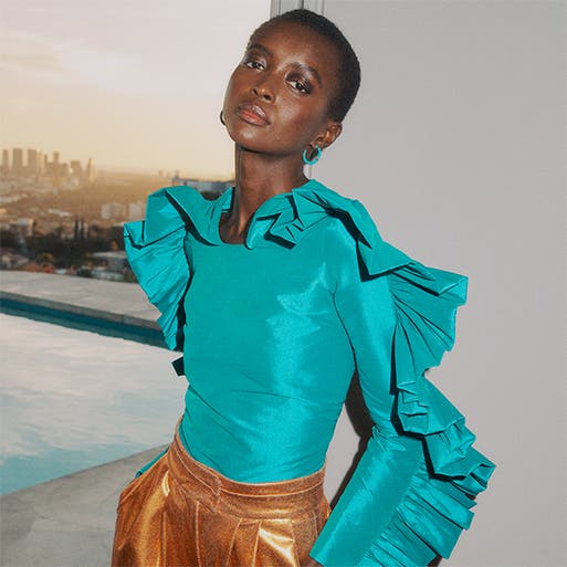 Model wearing a fitted turquoise top with ruffled sleeves and metallic copper shorts.