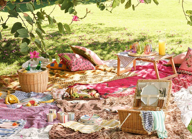 A picnic meal and colorful dishes spread out on blankets outside.