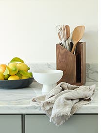 A bowl of lemons, white porcelain dish, kitchen towel and wooden utensil holder.