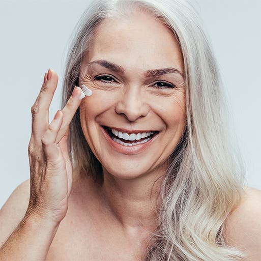 An older woman applying eye cream.