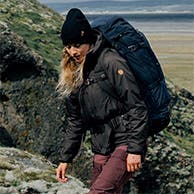 A woman wearing an outdoor jacket and beanie, hiking with a large backpack.