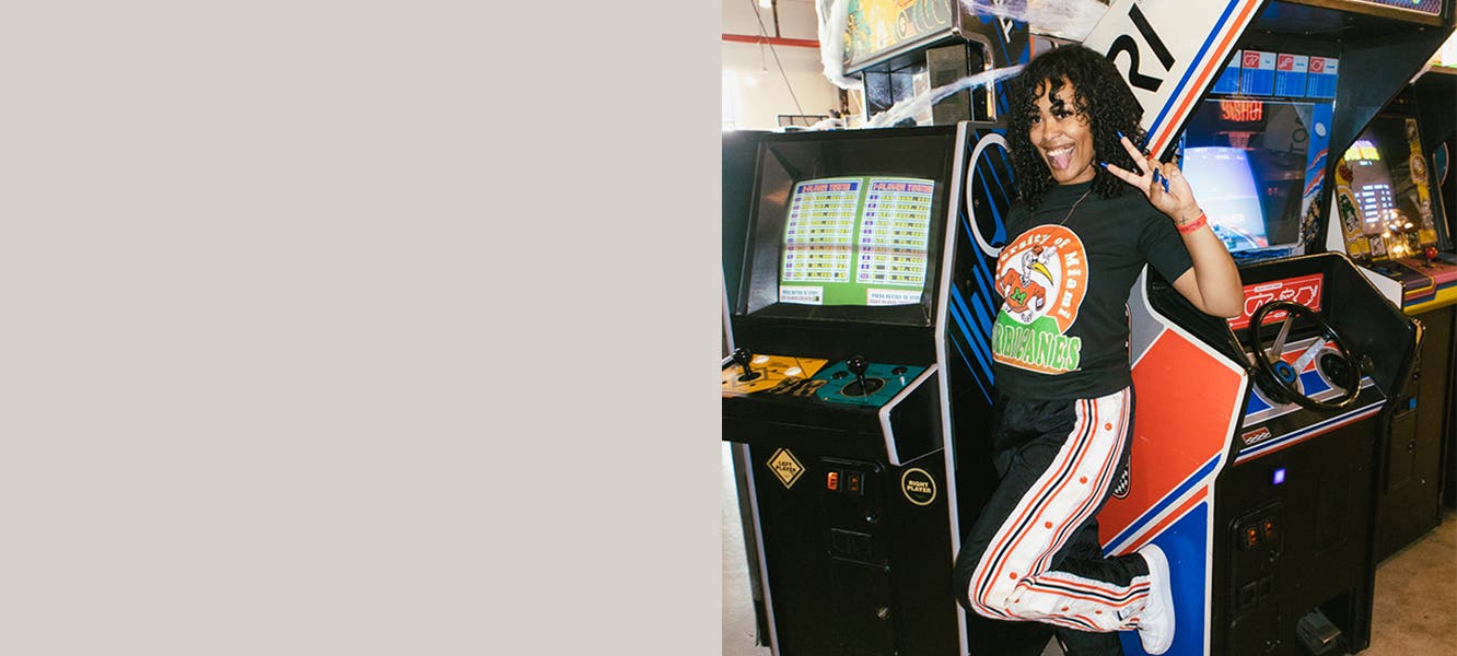 A woman poses in an arcade wearing a graphic tee with track pants.