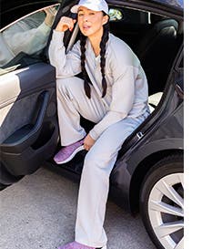 Woman lounging in loose grey top, pants and baseball cap.