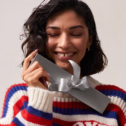 A woman wearing a red, white and blue striped sweater holding a silver Nordstrom gift box.