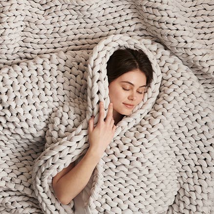 A woman wrapped in a thick knit blanket.