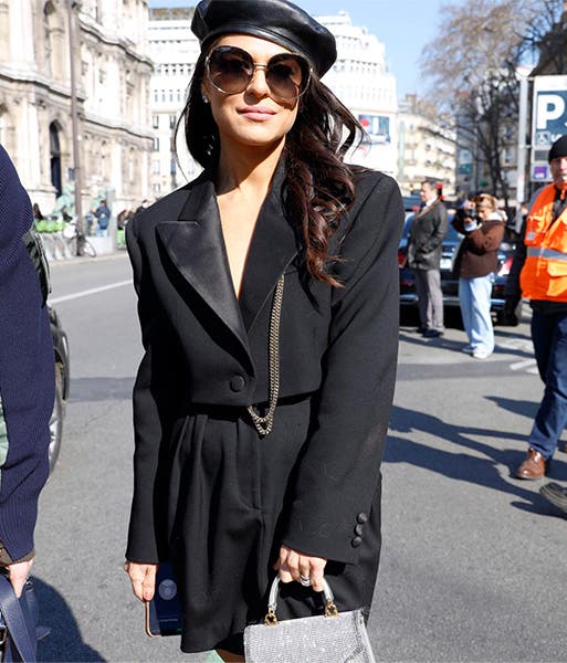 A woman wearing a black blazer dress, a black leather beret and oversized black sunglasses.