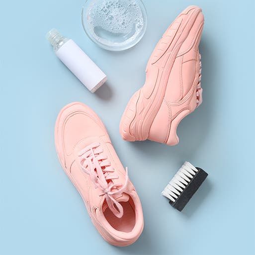 A pair of pink sneakers, a bottle of soap, a jar of water and a cleaning brush.