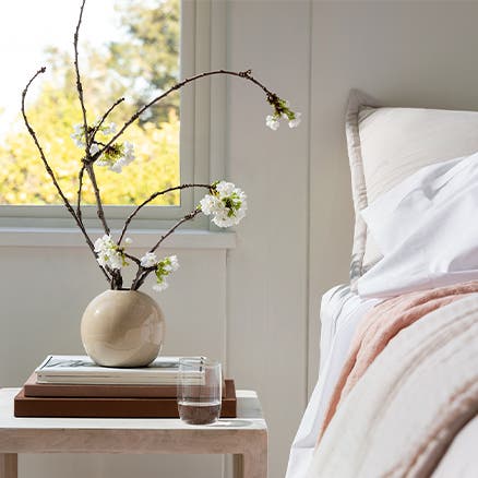 A neutral-toned ball-shaped vase holding floral branches on a nightstand.